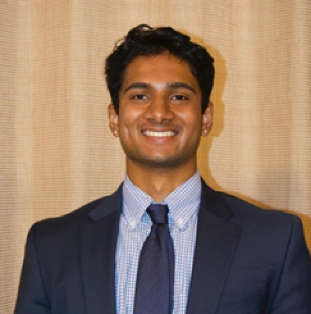 Shreyas in a blue suit and tie smiling looking at camera