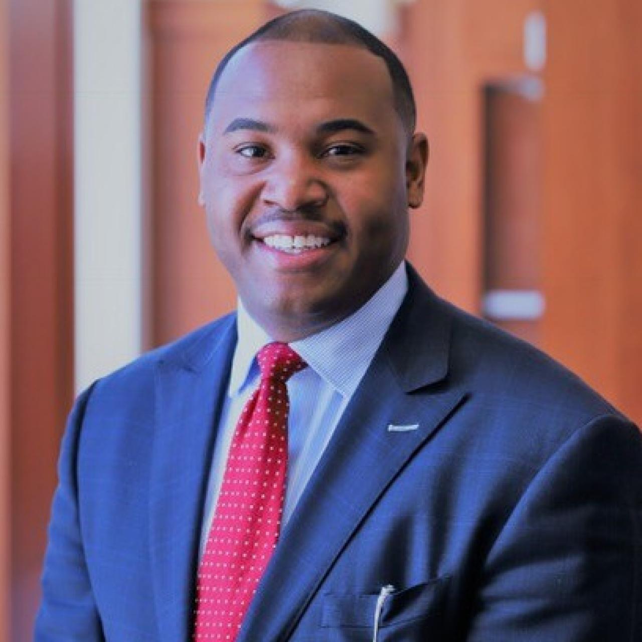 Trey Addison headshot wearing a blue suit and red tie, looking into the camera.