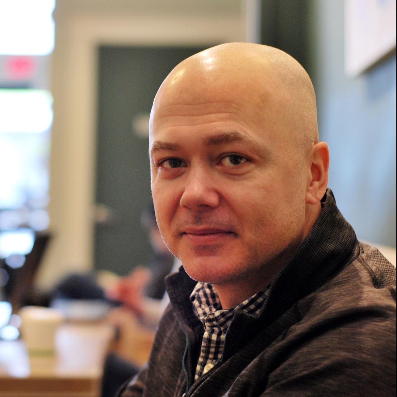 Image of Stephen Griffin sitting at a table wearing gray zip up and checkered collared shirt