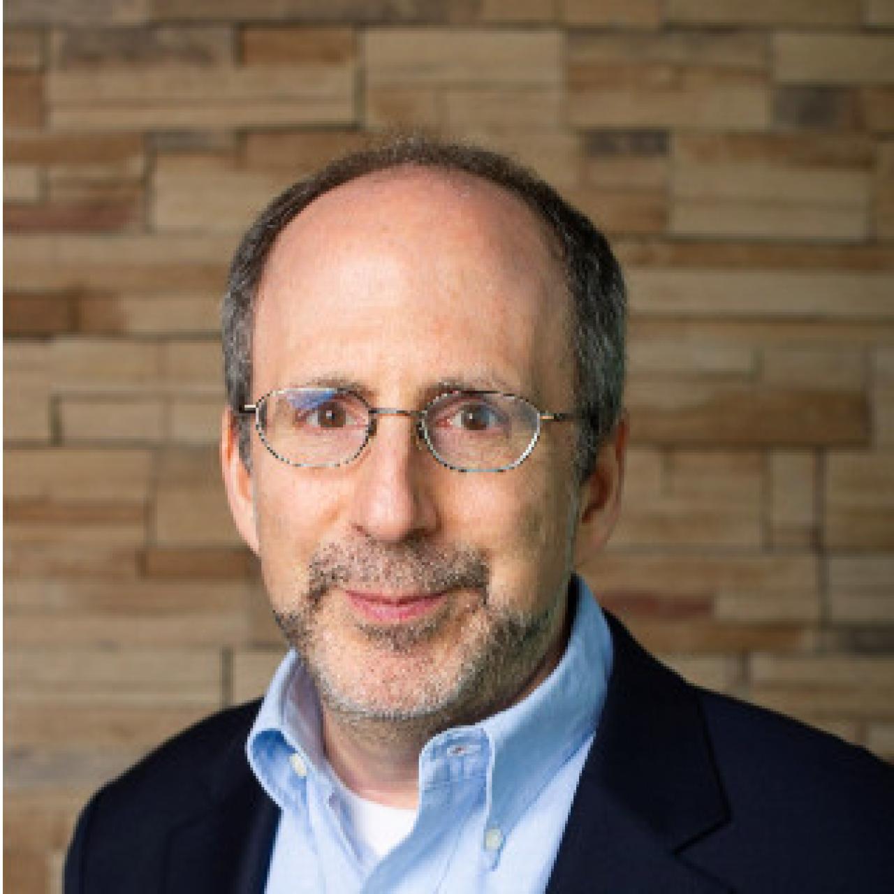 Image of Michael standing against brick wall wearing light blue collared shirt.