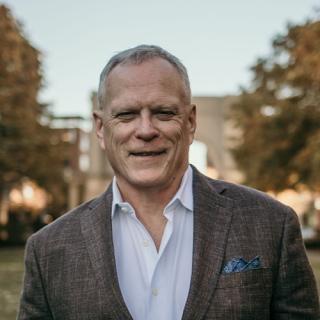 Image of Brian wearing a sport coat and collared shirt with trees in the background.
