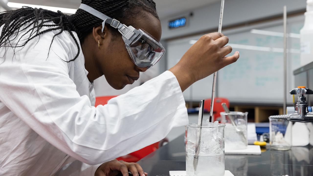 Woman in lab examining thermometer in beaker