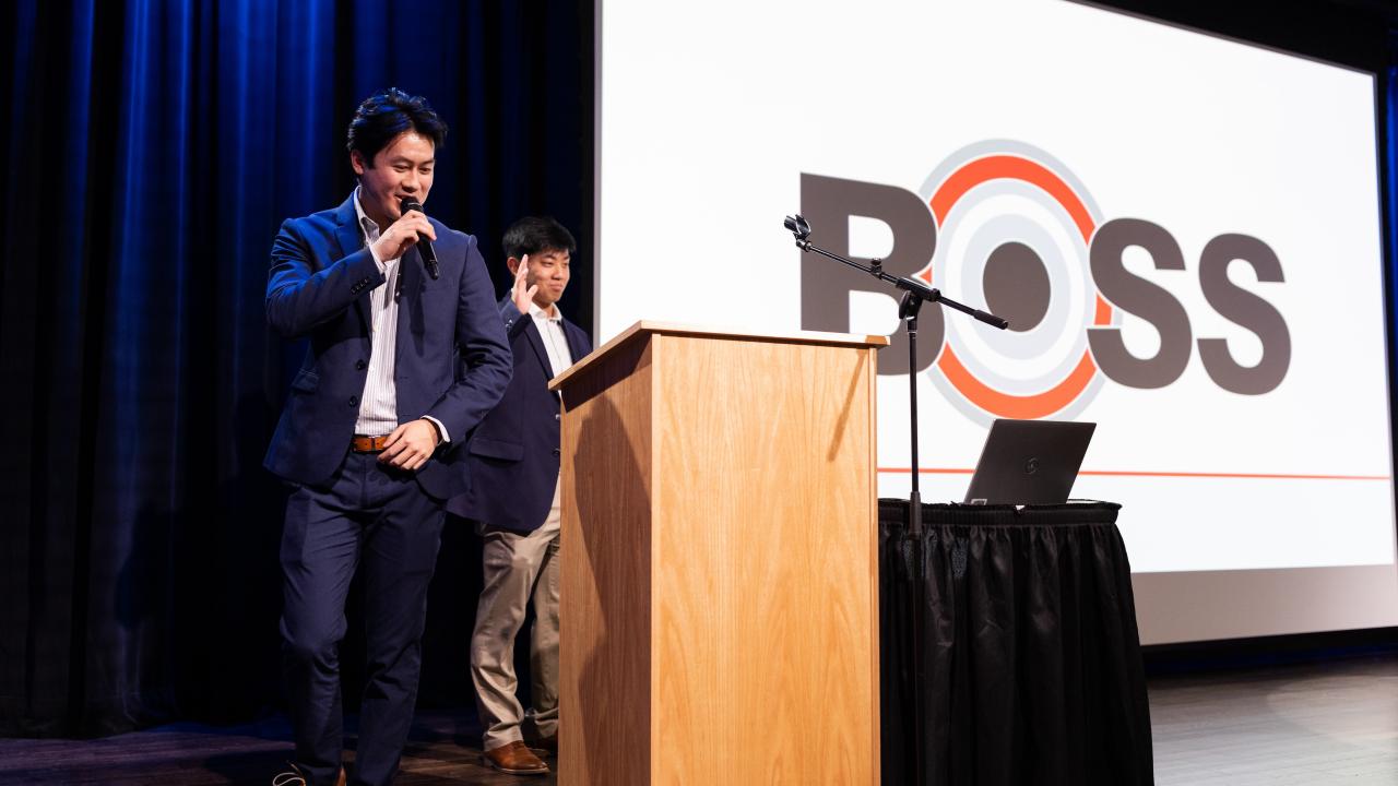 A student at BOSS enthusiastically presents on stage in a black suit