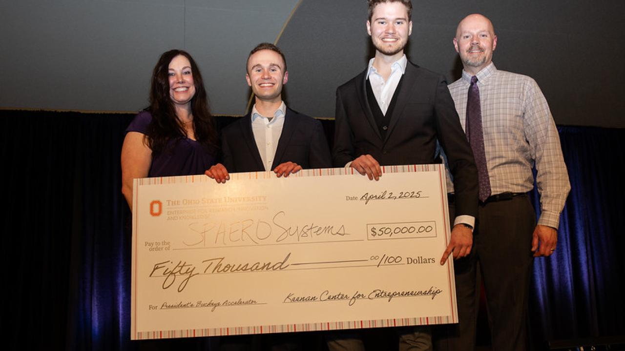 Four people smiling and standing holding up a large check.
