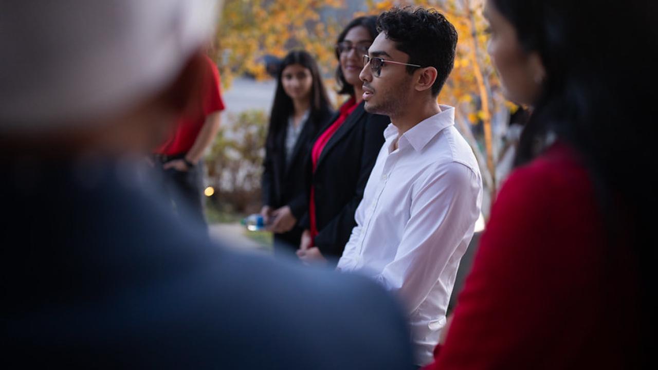 A person speaking outdoors surrounded by people watching and listening.